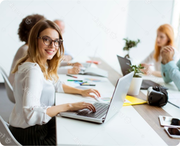 Kobieta w pracy z uśmiechem spogląda znad laptopa
